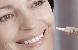 Mulher a aplocar um produto Eucerin na bochecha esquerda.