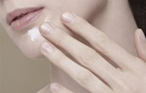 Mulher a aplicar creme no queixo.